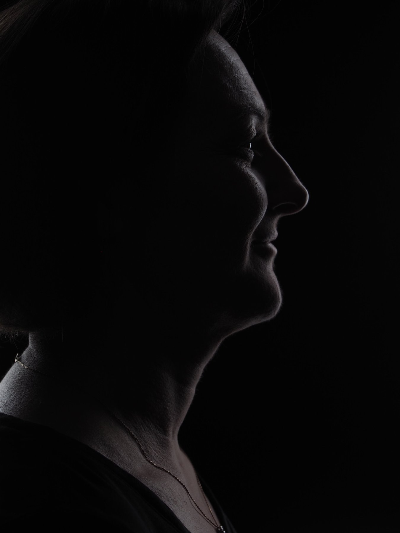 Low-Key-Portrait im Profil: Gesicht einer lächelnden Frau, nur von einem feinen Lichtsaum vor schwarzem Hintergrund konturiert