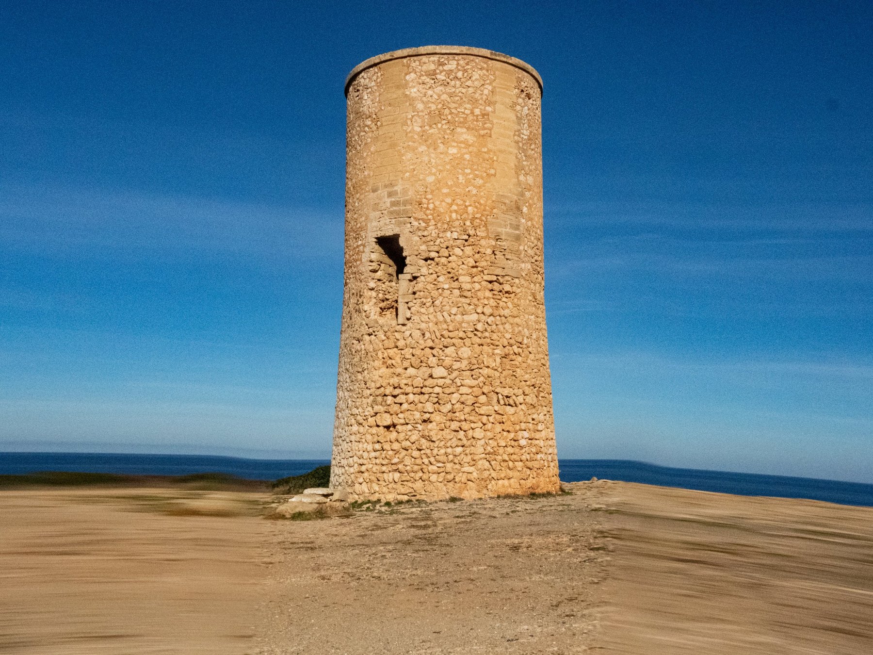 Alter Wachturm aus Naturstein auf einer Küstenklippe vor tiefblauem Himmel und Meer